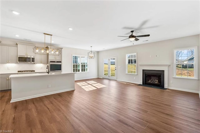 unfurnished living room with plenty of natural light, dark hardwood / wood-style floors, sink, and ceiling fan with notable chandelier