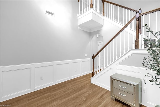 1604 Sunny Hill Way, Colfax, NC 27235 - stairs featuring a decorative wall, wood finished floors, wainscoting, arched walkways, and a high ceiling