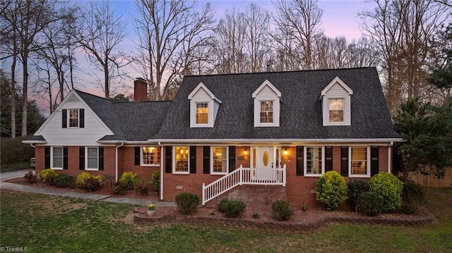 cape cod house featuring brick siding, a yard, and a chimney