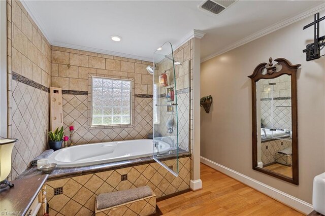 full bathroom featuring a relaxing tiled tub, wood finished floors, visible vents, ornamental molding, and tiled shower