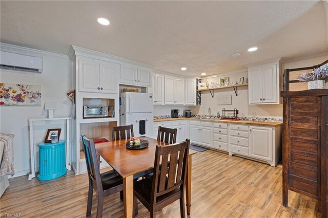 kitchen with a wall unit AC, light wood-type flooring, freestanding refrigerator, ornamental molding, and white cabinetry