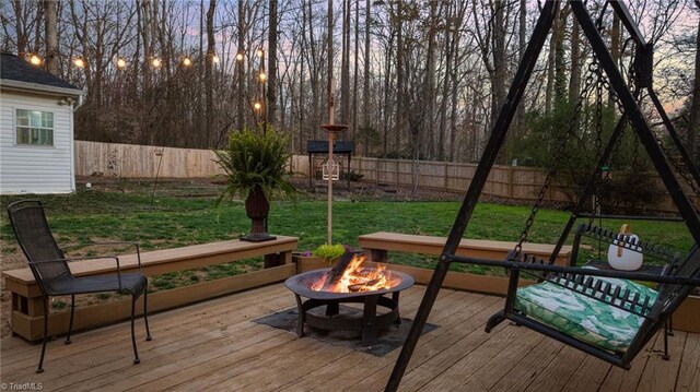 deck at dusk with a lawn, a fenced backyard, and a fire pit