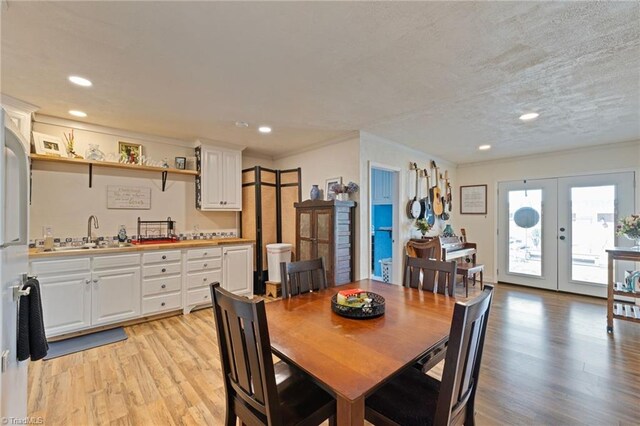 dining area with light wood-type flooring, wet bar, crown molding, and french doors