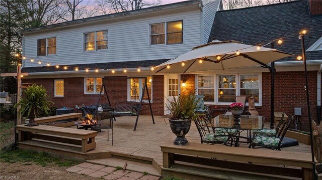 back of property with outdoor dining area, a wooden deck, central AC unit, brick siding, and a fire pit