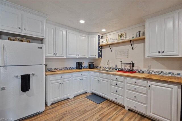 kitchen with freestanding refrigerator, butcher block counters, light wood-style floors, white cabinets, and a sink