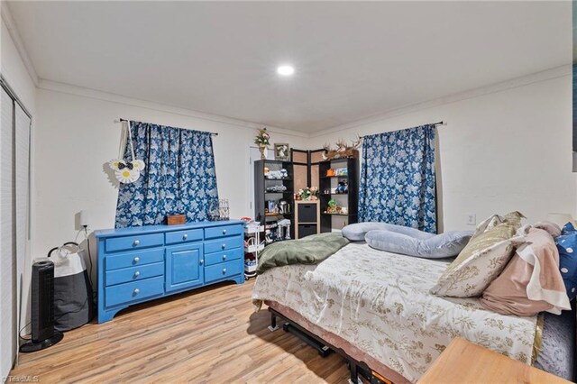 bedroom with light wood-style floors, ornamental molding, and a closet
