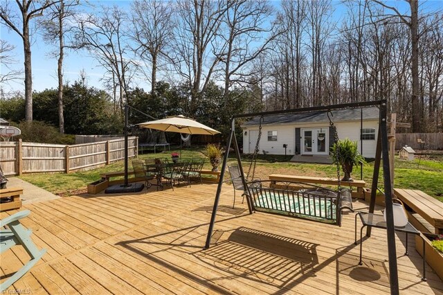 wooden deck with an outdoor structure, fence, french doors, a trampoline, and a yard