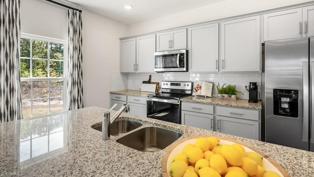 kitchen with light stone counters, stainless steel appliances, sink, and backsplash