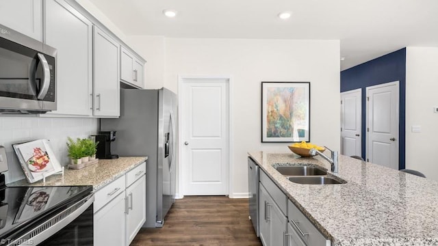 kitchen with sink, stainless steel appliances, dark hardwood / wood-style floors, light stone counters, and decorative backsplash