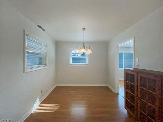 unfurnished dining area with a chandelier, visible vents, baseboards, and wood finished floors