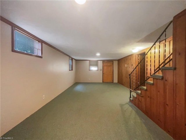 finished basement with carpet floors, wood walls, and stairway