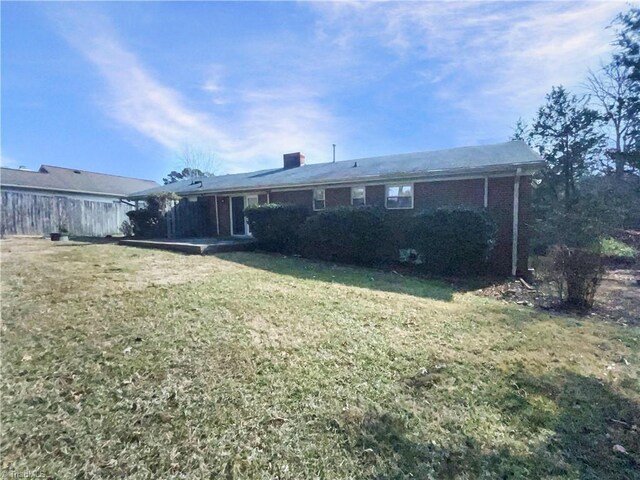 back of property featuring brick siding, a lawn, and fence