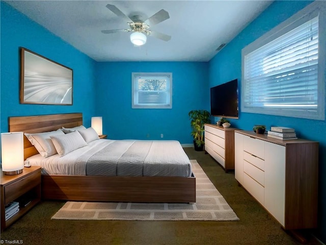 bedroom featuring a ceiling fan, dark colored carpet, multiple windows, and visible vents