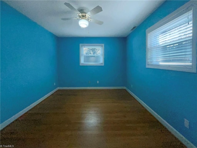 unfurnished room with a ceiling fan, visible vents, baseboards, and wood finished floors