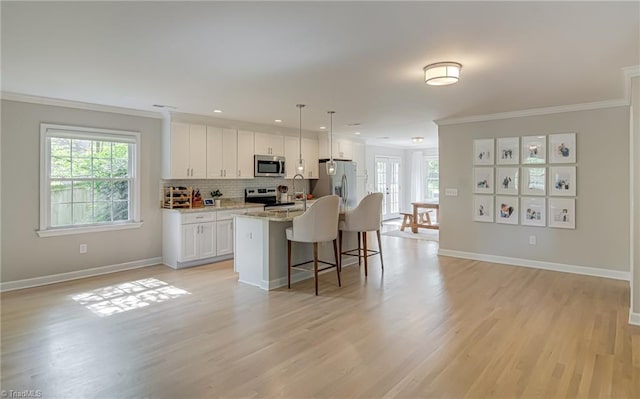 kitchen with appliances with stainless steel finishes, a breakfast bar area, ornamental molding, white cabinets, and light wood-type flooring