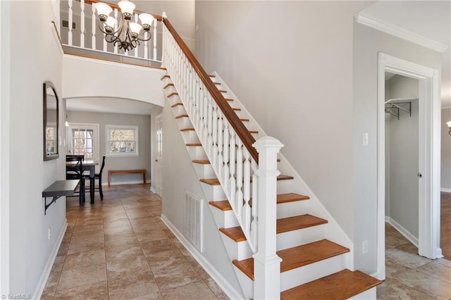 staircase with crown molding, a chandelier, and a high ceiling