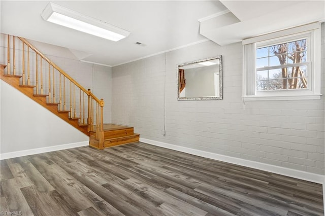 interior space featuring dark wood-type flooring, ornamental molding, and brick wall