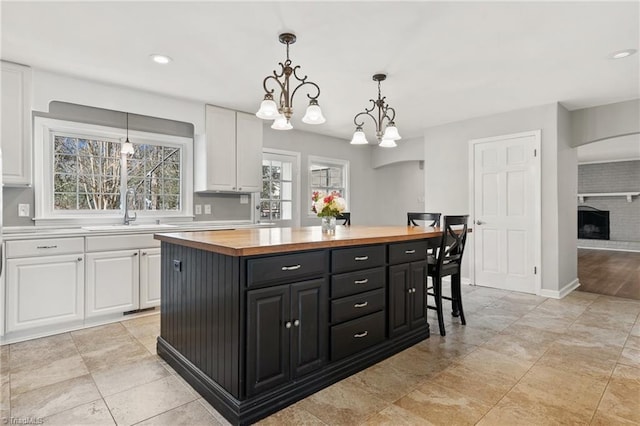 kitchen featuring sink, white cabinetry, a center island, wood counters, and decorative light fixtures