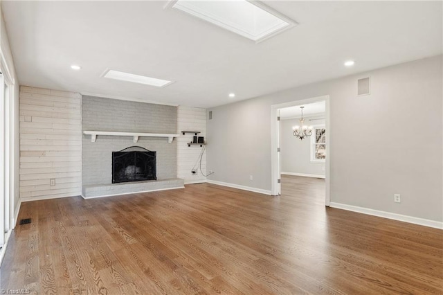 unfurnished living room with hardwood / wood-style flooring, a brick fireplace, a chandelier, and a skylight