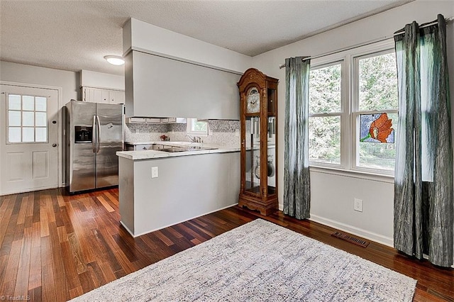 kitchen featuring kitchen peninsula, white cabinetry, stainless steel refrigerator with ice dispenser, dark hardwood / wood-style flooring, and decorative backsplash