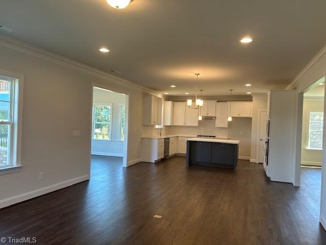 kitchen with pendant lighting, a kitchen island, crown molding, white cabinetry, and plenty of natural light