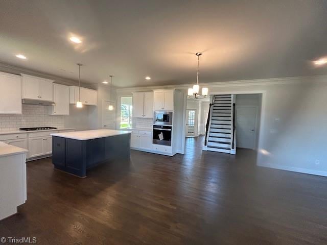 kitchen with white cabinetry, stainless steel appliances, hanging light fixtures, ornamental molding, and a center island