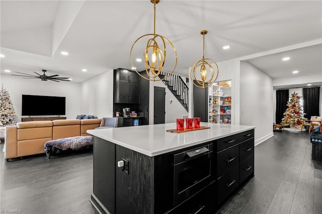 kitchen with decorative light fixtures, dark hardwood / wood-style flooring, ceiling fan with notable chandelier, and a kitchen island