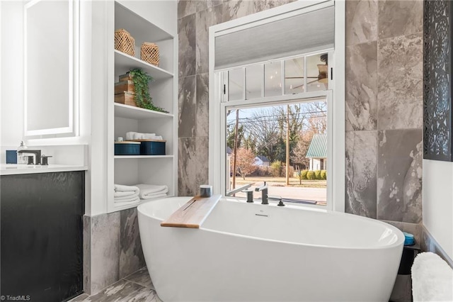 bathroom with tile walls, a tub to relax in, and vanity