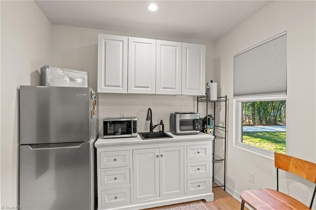 kitchen with white cabinets, appliances with stainless steel finishes, sink, and light hardwood / wood-style floors