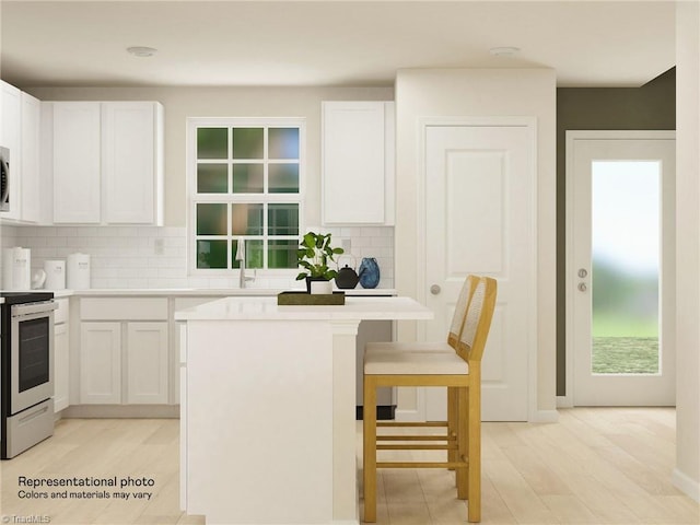 kitchen with a sink, white cabinets, a kitchen breakfast bar, electric stove, and backsplash