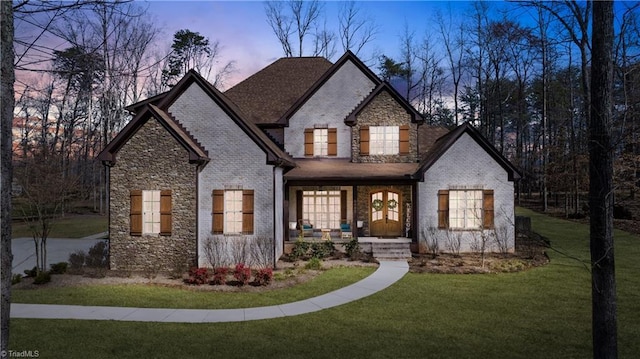 french country inspired facade with brick siding, covered porch, and a front yard