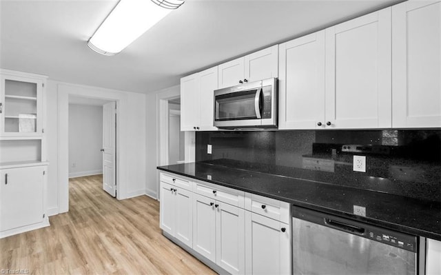 kitchen with white cabinets, stainless steel appliances, dark stone counters, and light hardwood / wood-style floors