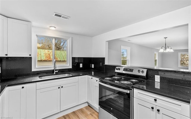 kitchen featuring backsplash, stainless steel electric range oven, sink, an inviting chandelier, and white cabinetry