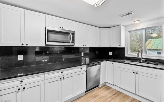 kitchen featuring sink, backsplash, appliances with stainless steel finishes, white cabinets, and light wood-type flooring