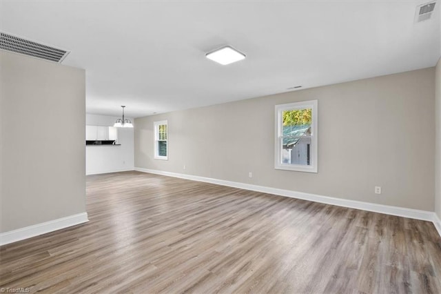 empty room with a wealth of natural light, light hardwood / wood-style floors, and a notable chandelier