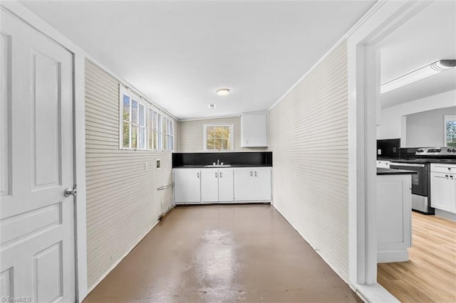 kitchen with white cabinets, sink, stainless steel electric stove, and brick wall