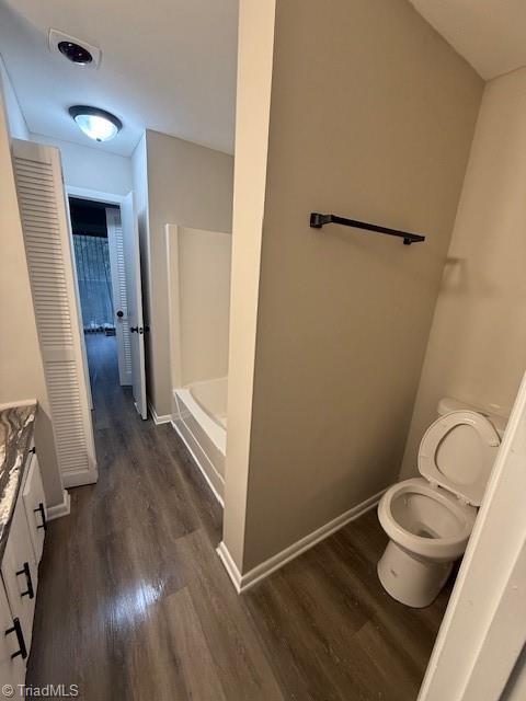 bathroom featuring baseboards, toilet, wood finished floors, and vanity