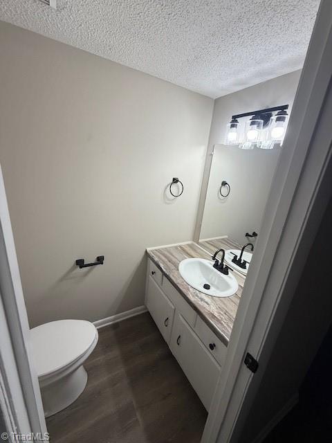 bathroom with toilet, a textured ceiling, wood finished floors, baseboards, and vanity