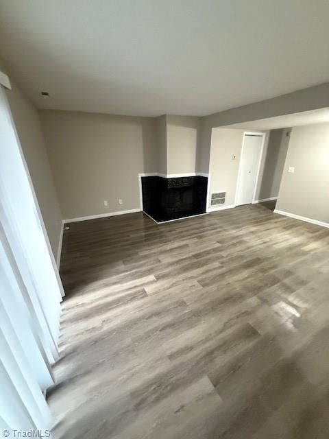 unfurnished living room featuring visible vents, a multi sided fireplace, baseboards, and wood finished floors