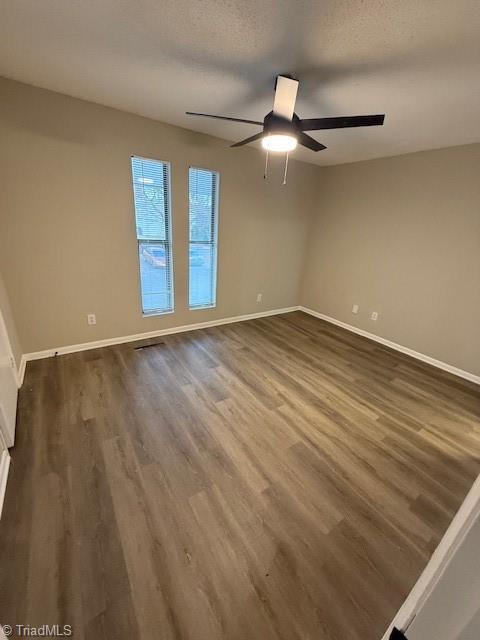 empty room with ceiling fan, a textured ceiling, dark wood-type flooring, and baseboards