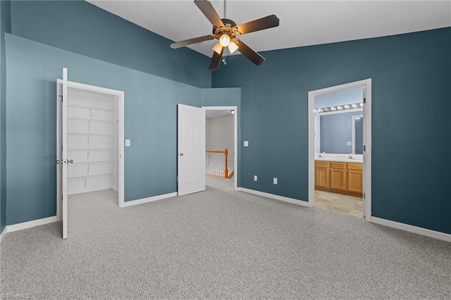 unfurnished bedroom featuring light carpet, ensuite bath, ceiling fan, a spacious closet, and a closet