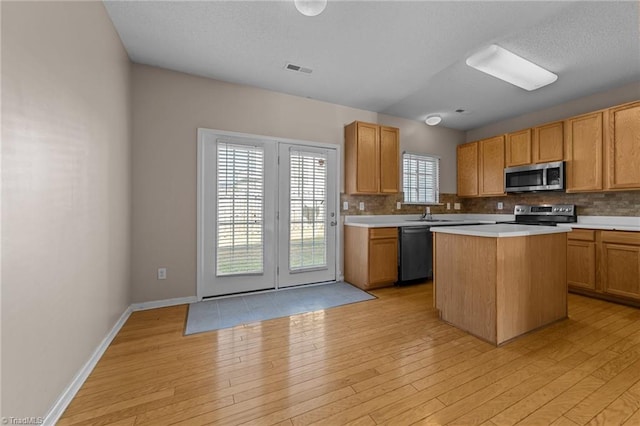 kitchen featuring backsplash, sink, light wood-type flooring, appliances with stainless steel finishes, and a kitchen island