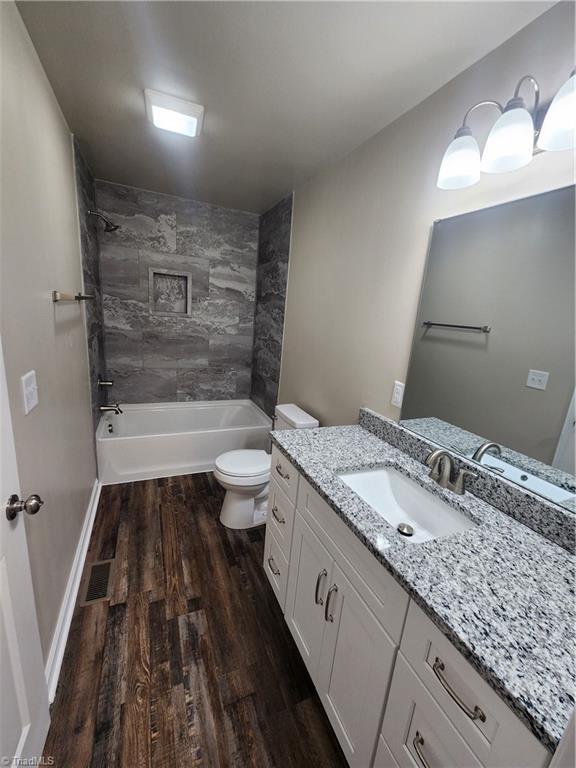 full bathroom with vanity, hardwood / wood-style flooring, toilet, and tiled shower / bath combo