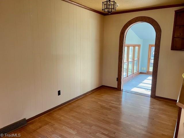 unfurnished room featuring light wood-style floors, arched walkways, ornamental molding, and baseboards