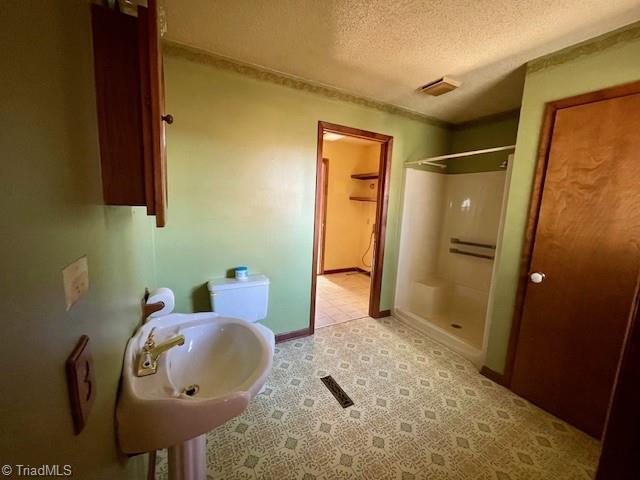 full bath featuring a stall shower, a sink, a textured ceiling, and baseboards