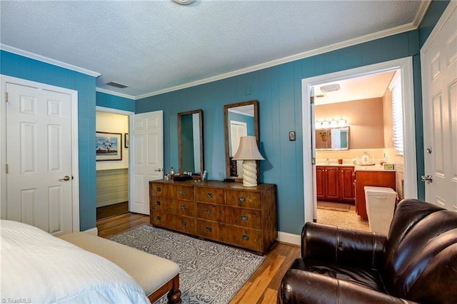 bedroom with crown molding, ensuite bath, light hardwood / wood-style floors, and a textured ceiling