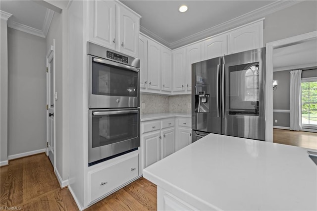 1203 Westminster Dr, Greensboro, NC 27410 - kitchen featuring appliances with stainless steel finishes, crown molding, white cabinetry, light wood finished floors, and decorative backsplash