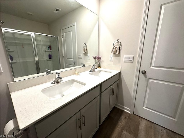 full bath with double vanity, a sink, a stall shower, and wood finished floors