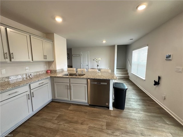 kitchen featuring dishwasher, a sink, a peninsula, dark wood-type flooring, and light stone counters