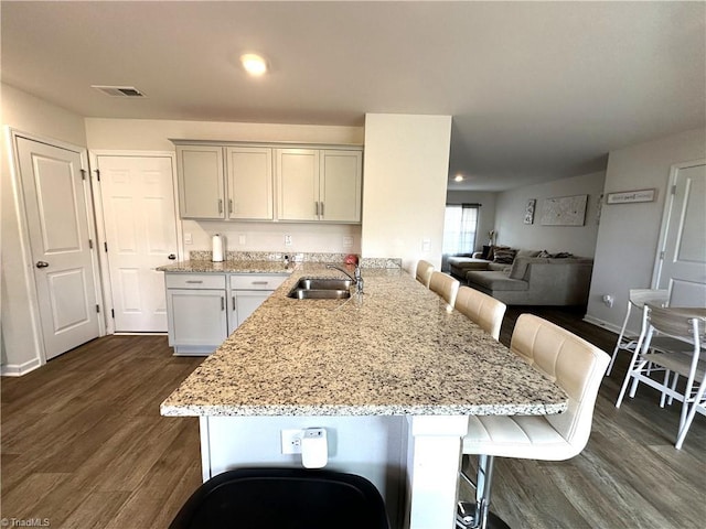 kitchen featuring dark wood-type flooring, a kitchen bar, visible vents, light stone counters, and a sink